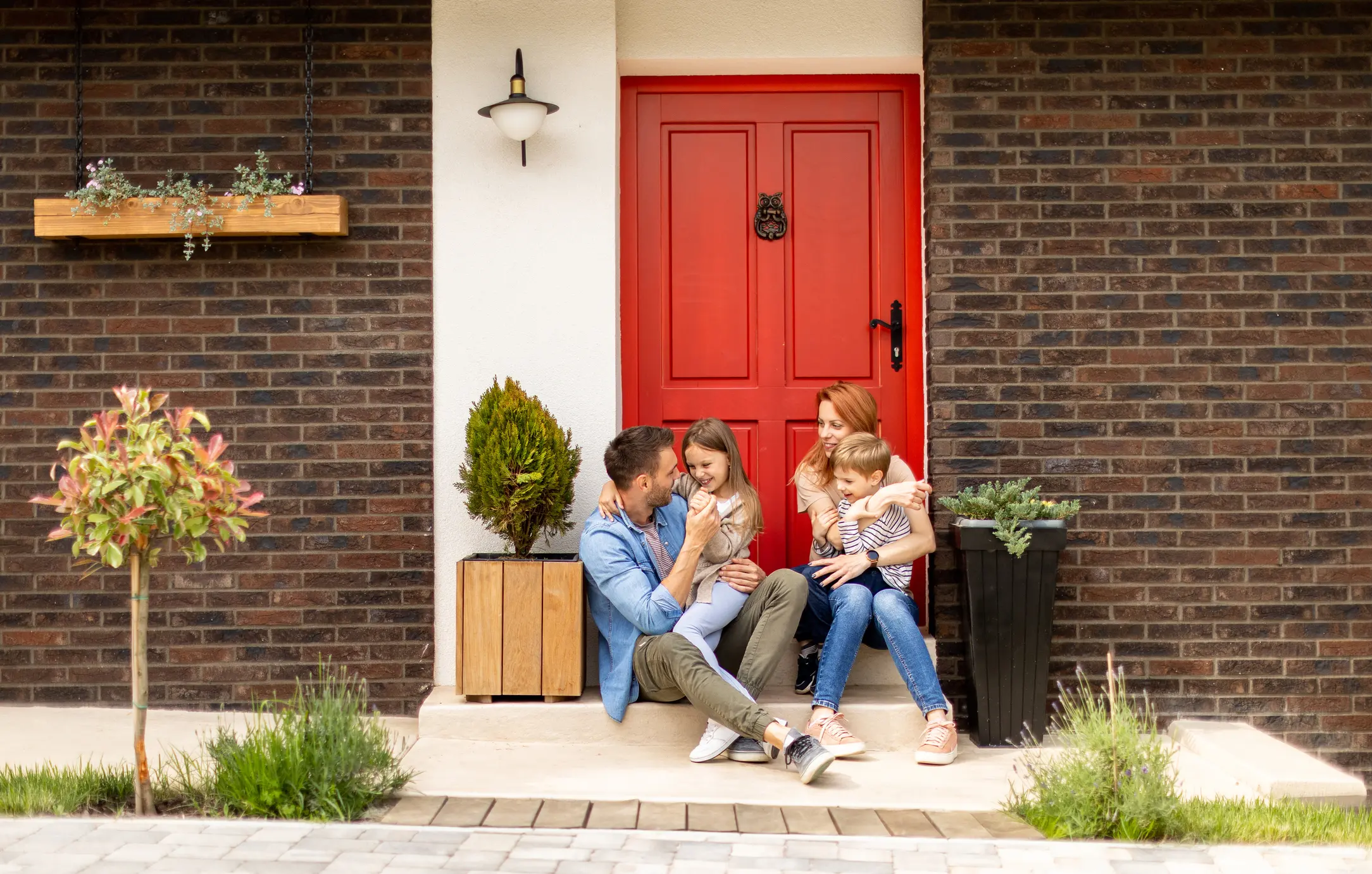 Family with a mother, father, son and daughter sitting outside on steps of a front porch of a brick house